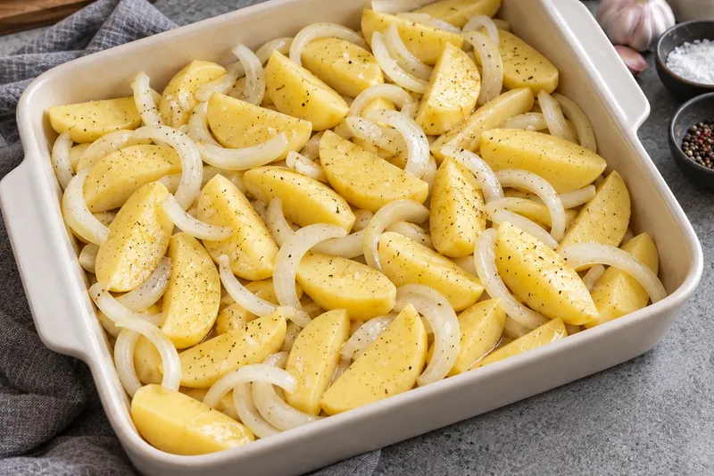 Курица в духовке с картошкой, шаг 3: Нарежьте картофель дольками, лук — полукольцами. Перемешайте с маслом и солью, выложите в…